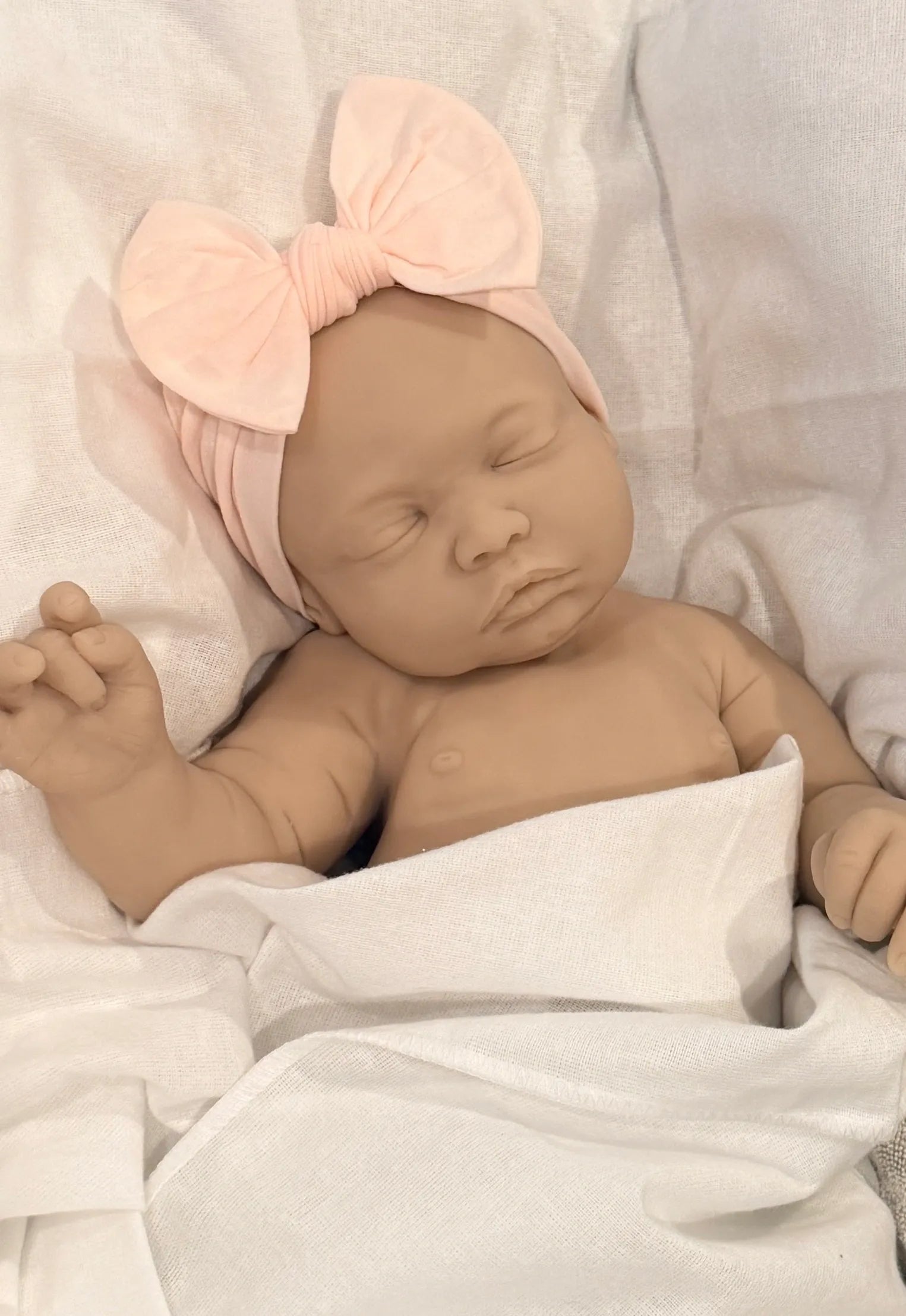 Newborn baby doll wrapped in a blanket with a pink headband.