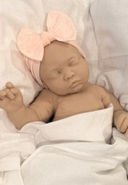Newborn baby doll wrapped in a blanket with a pink headband.