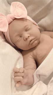 Newborn baby sleeping peacefully with a pink headband on a soft beige background